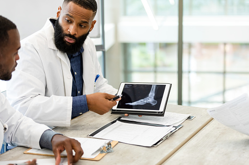 Two male orthopedic surgeons discuss an x-ray displayed on a digital tablet of a patient's foot.