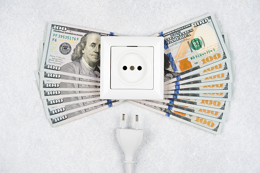 White socket with plug with many 100 dollars banknotes over light background. Concept of increasing prices for electricity in the world. High energy cost, world energy crisis concept