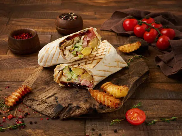 Shawarma chicken roll in a pita with fresh vegetables and cream sauce on wooden background. Selective focus