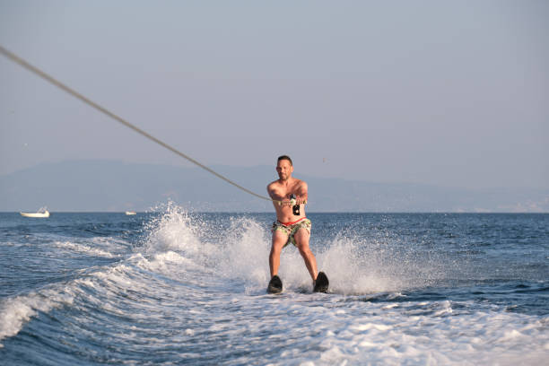 Mature man waterskiing across a lake... dips his hand into the water to create spray.