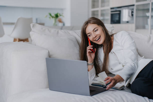 Excited blonde caucasian woman in white jacket and black pants laughs makes video call looks at screen of laptop toothy smiles wide sits on cozy sofa. Successful Italian female gets great news. emocionada mujer rubia caucásica con chaqueta blanca y pantalones negros se ríe hace que la videollamada mire la pantalla de la computadora portátil con dientes sonríe ampliamente se sienta en un acogedor sofá. la exitosa mujer italiana recibe una gra