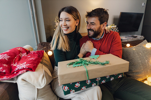 Couple sitting in the living room and celebrating Christmas holidays and holding gifts