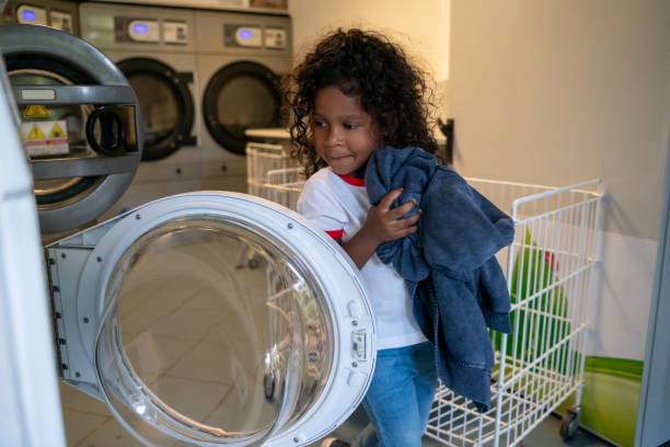 istock Child loading dirty clothes into a washer at a launderette 1441987004