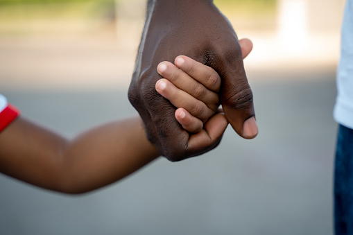 Cropped photo of an adult African American male person holding a child by the hand during the stroll