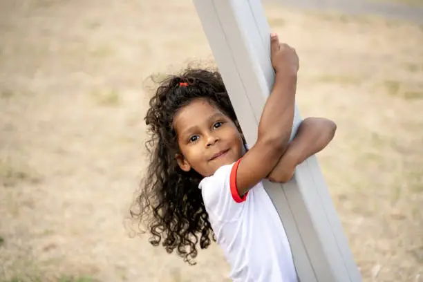 Cute curly-haired child holding on to the metal post and looking in front of her