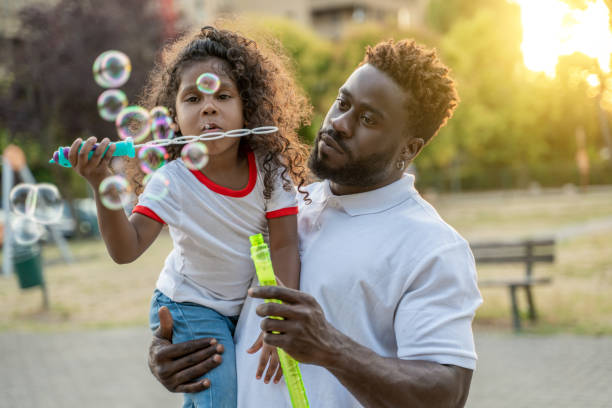niña jugando el juego de burbujas en los brazos de su padre - bubble child bubble wand blowing fotografías e imágenes de stock
