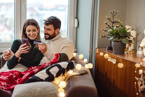 Couple sitting on the sofa in the living room and using mobile phone