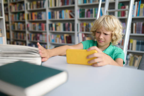 istock Blonde boy sitting in the library and spanding time online 1441990202