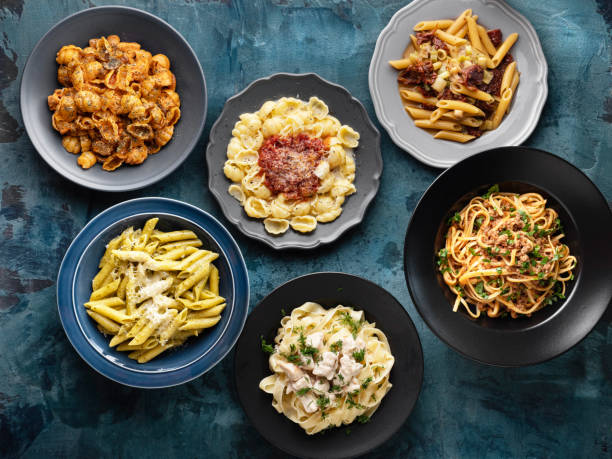 背景にさまざまな種類の調理済みパスタと麺、パスタ、ヌードル、マカロニ、パスタのバリエーション、調理テーブルの上のさまざまなパスタのコレクション - pasta directly above fusilli food ストックフォトと画像