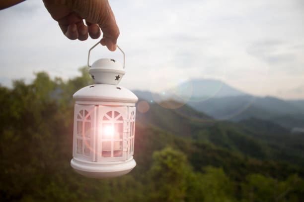 istock White lantern in hand light in hand on a mountains background. 1441993323