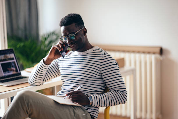 istock Smiling Businessman Talking On A Mobile Phone And Writing Notes At Home 1441994373