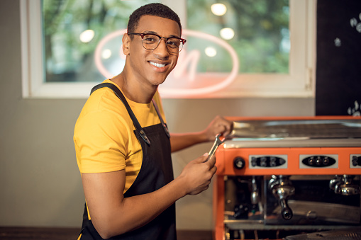 Waist-up portrait of a cheerful repairman with the spanner in the hand standing at the coffeemaker