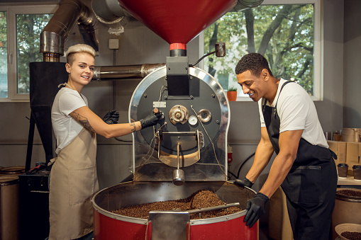 Smiling young roast master and her colleague determining together the roast degree of coffee beans