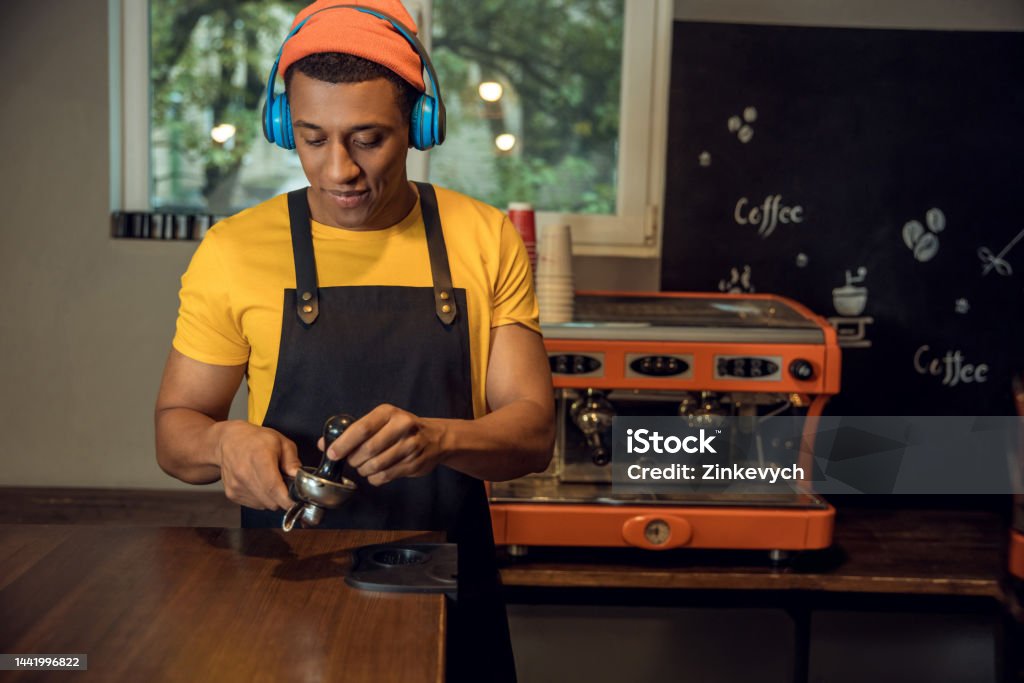 Professional barista making a caffeinated beverage to music Calm focused young man in the wireless headphones tamping the coffee grounds into the portafilter basket using the coffee tamper 30-34 Years Stock Photo