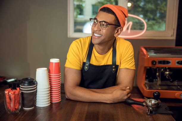 istock Smiling joyous young barista in his workplace 1441996827
