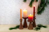 Four candles on wooden stands, three ar lit for the third Advent, pine branch decoration, light wooden board and rustic plaster background, copy space, selected focus