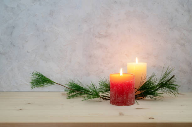 Two candles lit for the second Advent, pine branch as a simple, minimal decoration on a light wooden board against a rustic plaster wall, large copy space, selected focus stock photo