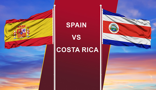 Spain vs. Costa Rica two flags on flagpoles and blue cloudy sky background.Soccer matchday template