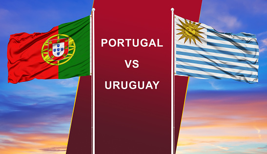 Portugal vs. Uruguay two flags on flagpoles and blue cloudy sky background.Soccer matchday template