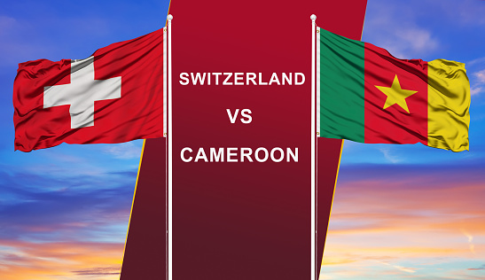 Switzerland vs. Cameroon two flags on flagpoles and blue cloudy sky background.Soccer matchday template