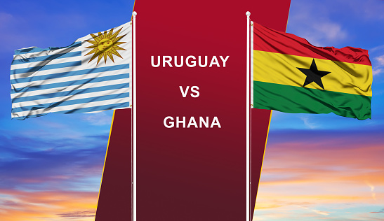 Uruguay vs. Ghana two flags on flagpoles and blue cloudy sky background.Soccer matchday template