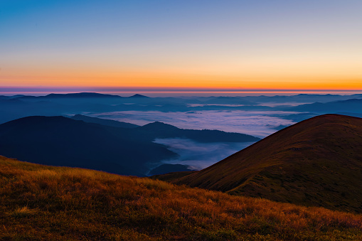 Dawn in the mountains. Orange sky above the clouds in the valley