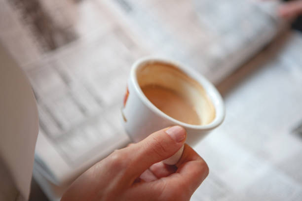 A white cup filled with creamy espresso on a wooden tray, placed on a white duvet with newspapers in the background. Clean, minimalistic composition with plenty of negative space. Perfect for a cozy, relaxed morning vibe