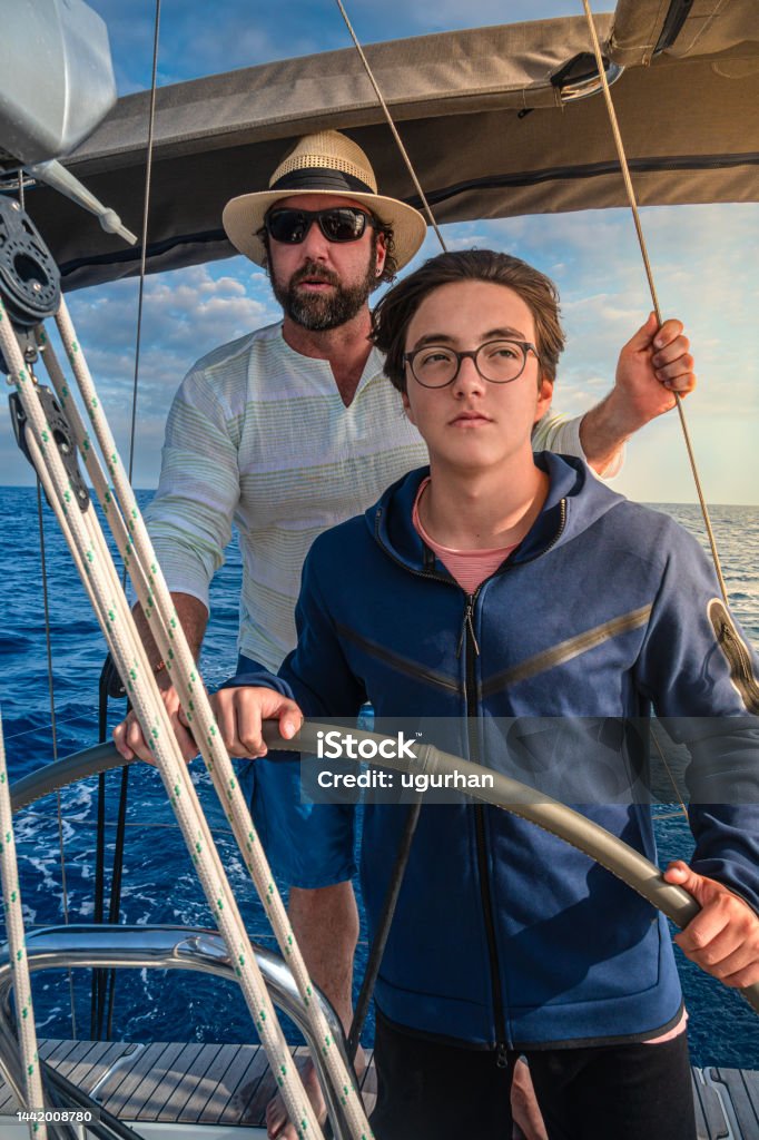 A father teaches his son to sailboat and guides him. Activity Stock Photo