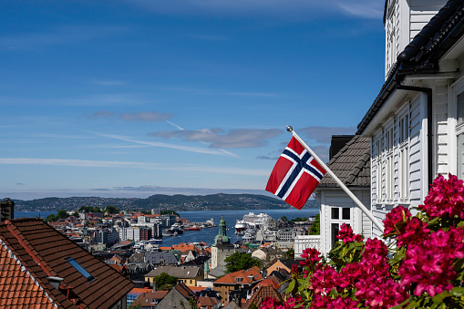 The Norwegian flag is placed on the facade of the house in Bergen, behind the flag you can see the city of Bergen with the fjord