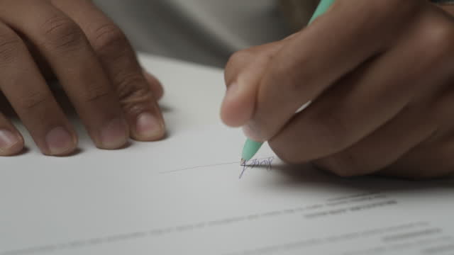 Hand puts signature on paper document. Man signing agreement, close up.