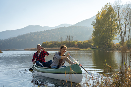 Two smiling couples on a joint trip with canoes on the autumn-colored Cerknica river. Dressed in casual clothes, they take selfies, laugh and enjoy the good mood on the water.