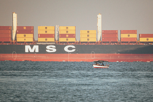 View of a fisherman boat near a giant container ship.\nCaptured in Izmir Gulf, Turkiye on 09/11/2022.