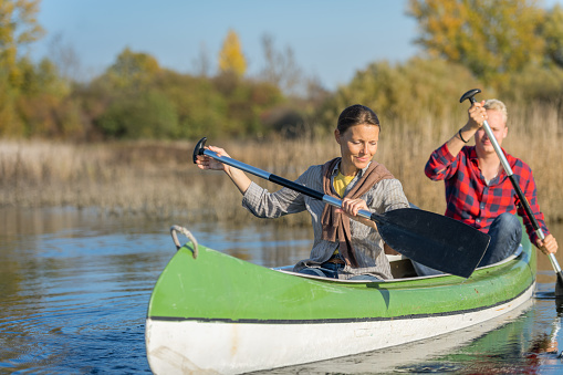 Two smiling couples on a joint trip with canoes on the autumn-colored Cerknica river. Dressed in casual clothes, they take selfies, laugh and enjoy the good mood on the water.