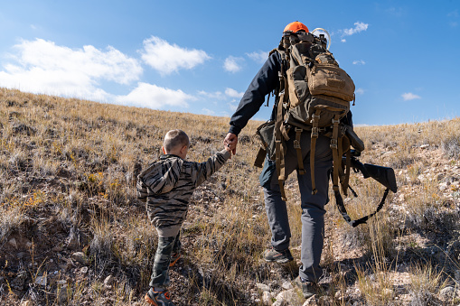 Wyoming, USA - October 7, 2022: Father and son walk in the sagebrush looking for deer during a child's first hunting trip. Holding hands