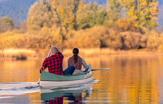Two smiling couples on a joint trip with canoes on the autumn-colored Cerknica river. Dressed in casual clothes, they take selfies, laugh and enjoy the good mood on the water.