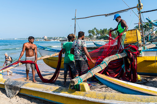Galle, Sri Lanka - November 15, 2019: local fishermen are preparing nets on the beach, before sailing and fishing in the ocean.
