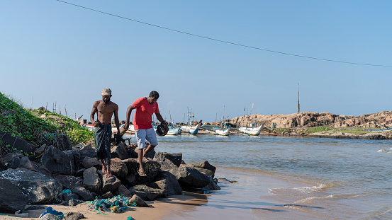 Galle, Sri Lanka - November 15, 2019: local men are walking down the rocks to the beach on the shore of the Atlantic Ocean on a hot day.