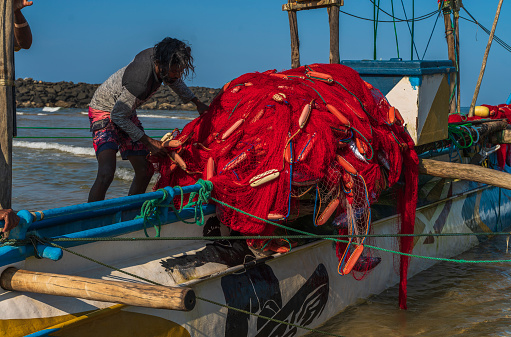 Galle, Sri Lanka - November 15, 2019:  local fisherman is getting ready for sailing and fishing at the Pacific Ocean on the motorboat. He is cheking the fishing net.