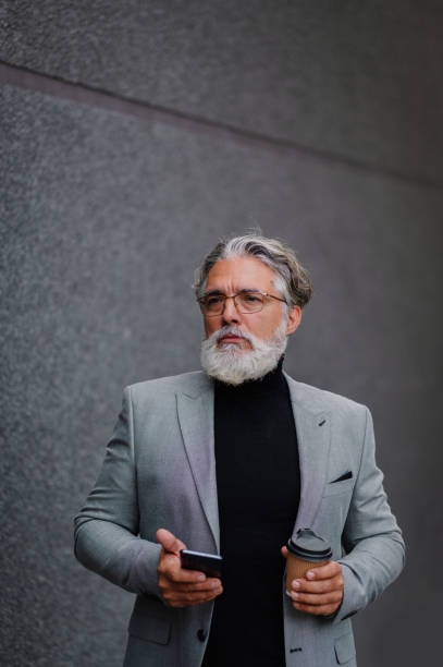 istock Senior businessman standing outside and using smartphone and drinking coffee 1442034125