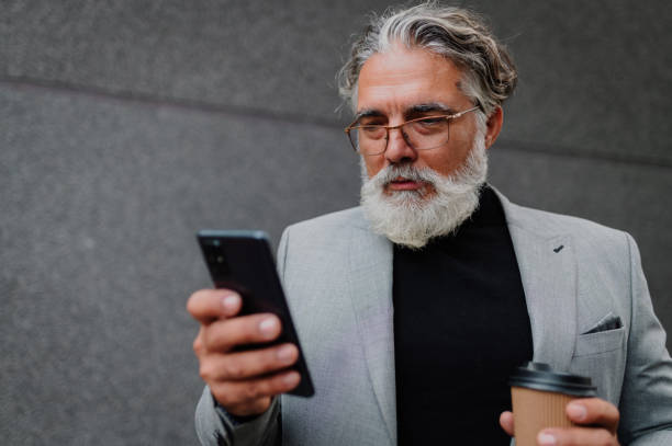 istock Senior business man standing outside while using smartphone and drinking coffee 1442034130