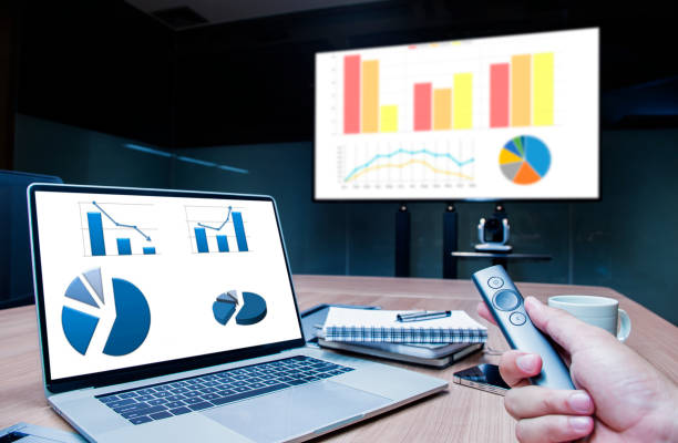 istock Businessman hand hold remote control slide with mock up chart slide show presentation on display laptop and television in meeting room 1442064304