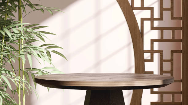 Modern, minimal round wooden table podium with bamboo and Chinese pattern design partition in dappled sunlight on beige wall