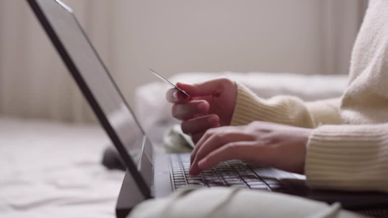 Woman sitting on the bed making payment online using a credit card and laptop