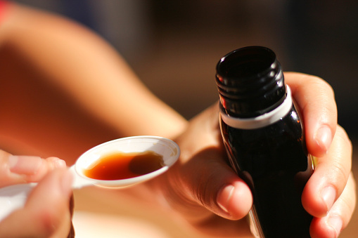 the hand holding the bottle will pour cough syrup onto a plastic spoon. health concept, medicine, syrup medicine, spoon. close up