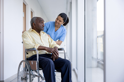 Latin American nurse talking to a senior man in a wheelchair at the hospital - healthcare and medicine concepts