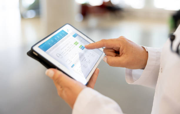 médico usando una aplicación móvil en una tableta en el hospital - informe médico fotografías e imágenes de stock