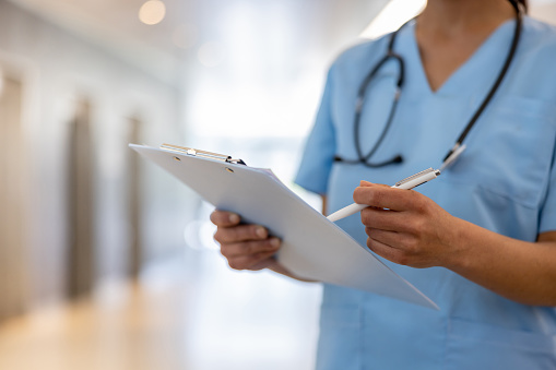 Close-up on a nurse holding a clipboard and writing on a medical chart at the hospital - healthcare and medicine concepts