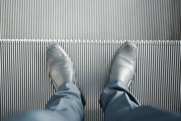 Man with pair of leather shoes standing on move up escalator, escalator down.