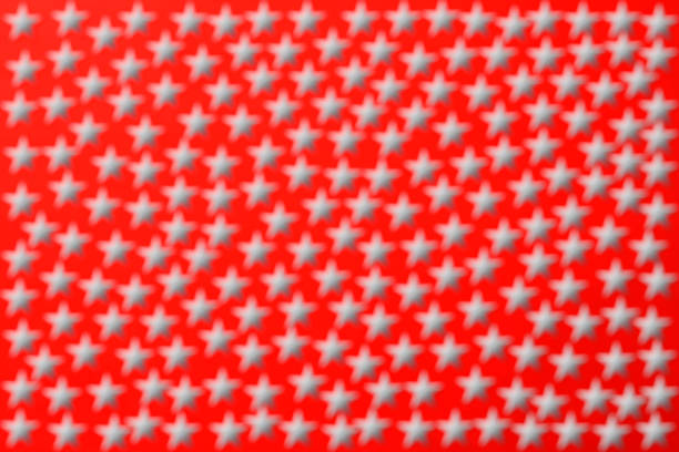 Overhead shot of defocused many silver stars on red background.