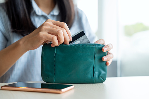 Midsection Of An Asian Woman Taking A Credit Card Out From Her Purse Over Table